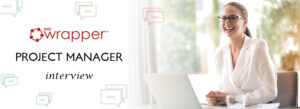 A smiling professional woman in a white blazer and glasses sitting with a laptop, titled "Project Manager Interview" with the qmsWrapper logo.