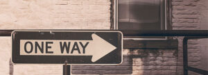 A "One Way" directional sign on a brick wall, serving as a metaphor for the singular, integrated path to compliance provided by qmsWrapper’s unified Project, Risk, and Document Management DNA.