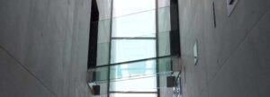 A modern glass walkway bridge between two concrete walls, symbolizing the bureaucratic glass ceiling and ISO 13485:2016 compliance barriers faced by medical device startups.